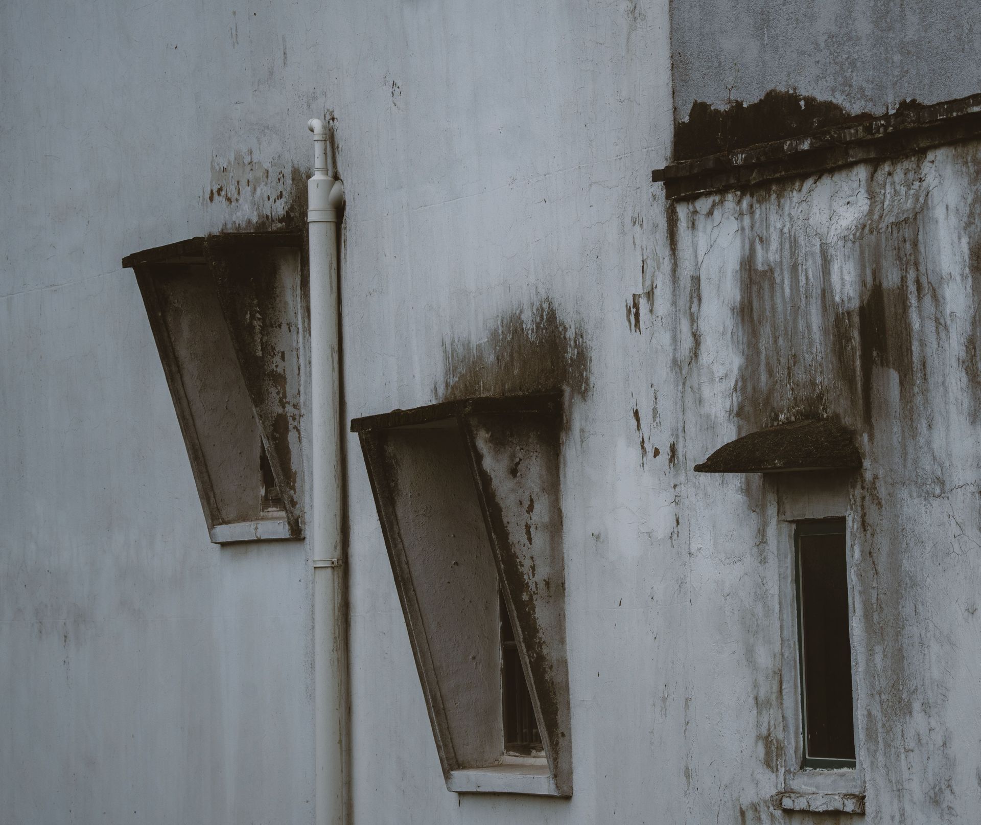 Weathered white wall with three narrow, dark window openings and peeling stains