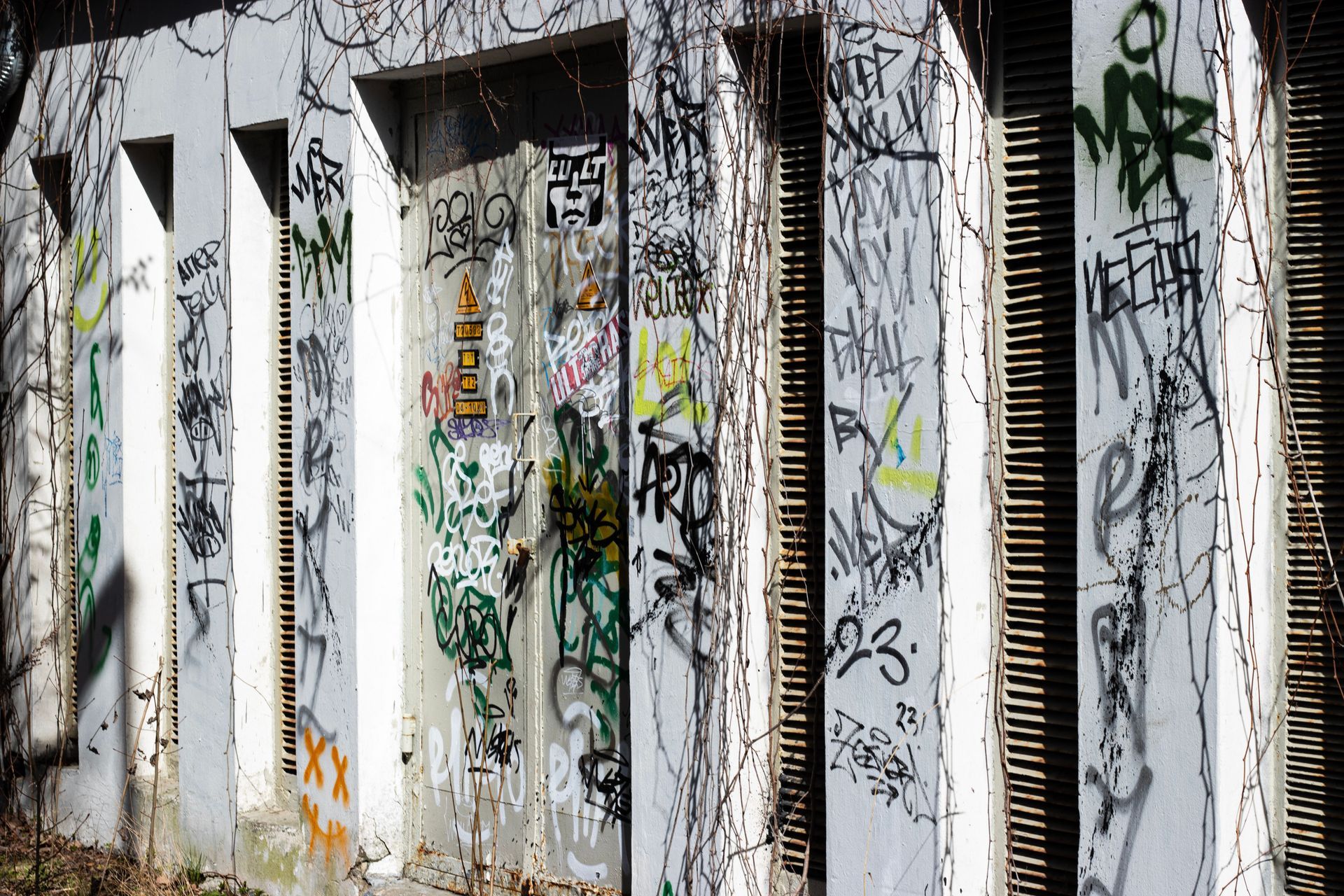 Graffiti-covered white wall panels with narrow vertical slats and peeling paint in an urban setting