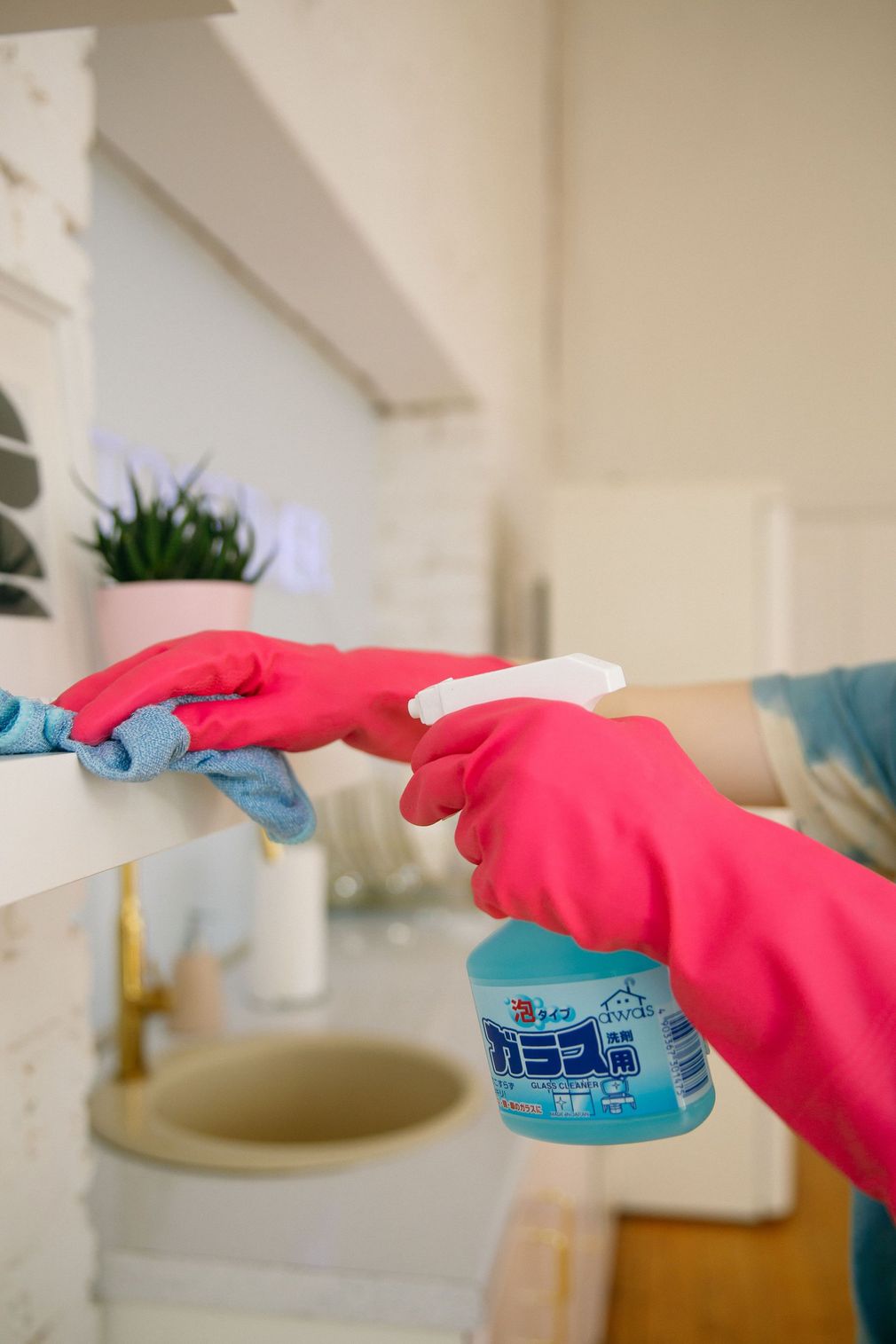 Person in pink gloves spraying a sink with cleaning spray in a bathroom