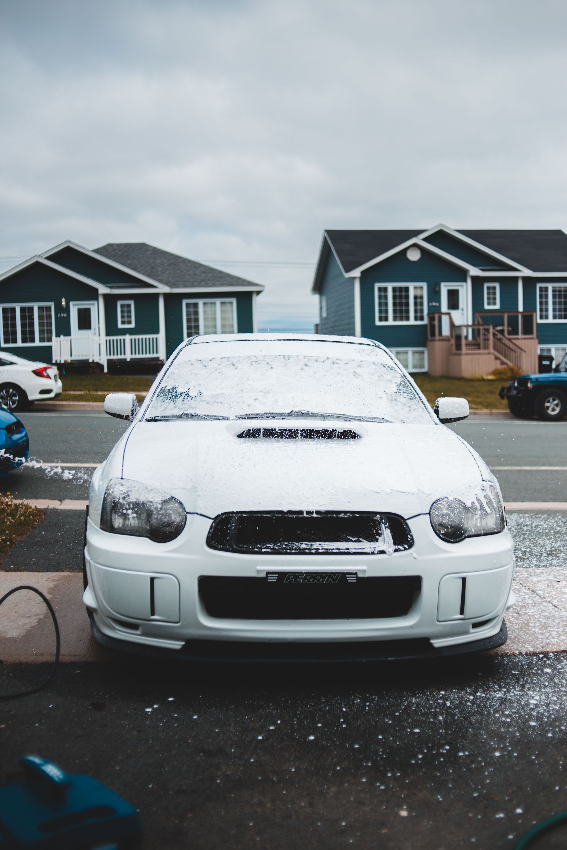 White car covered in snow parked in a residential driveway on a cloudy day