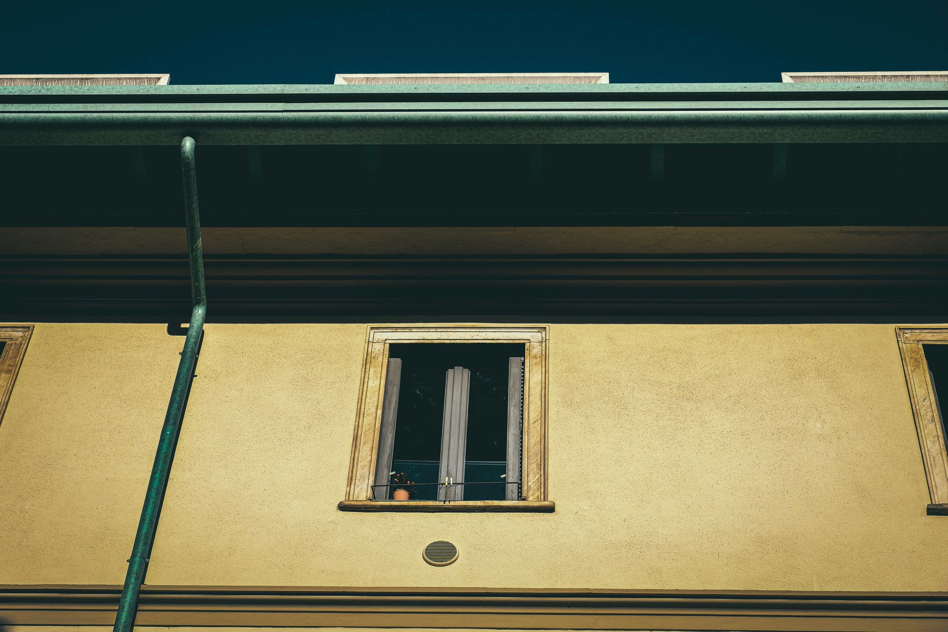 Yellow building facade with a narrow open window and dark green roof trim