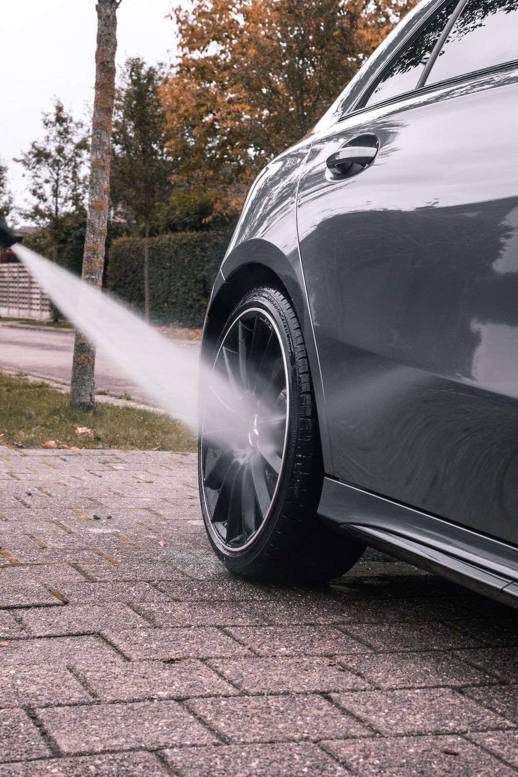 Black car spraying water from its rear wheel on a wet brick driveway