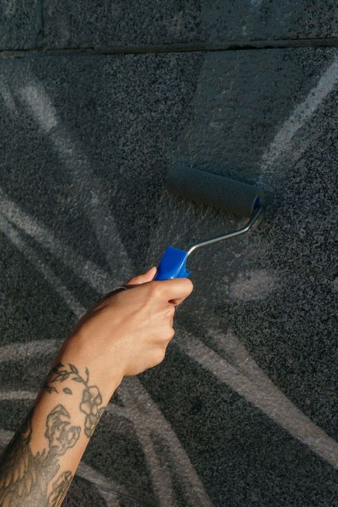 Hand painting a dark wall with a blue paint roller