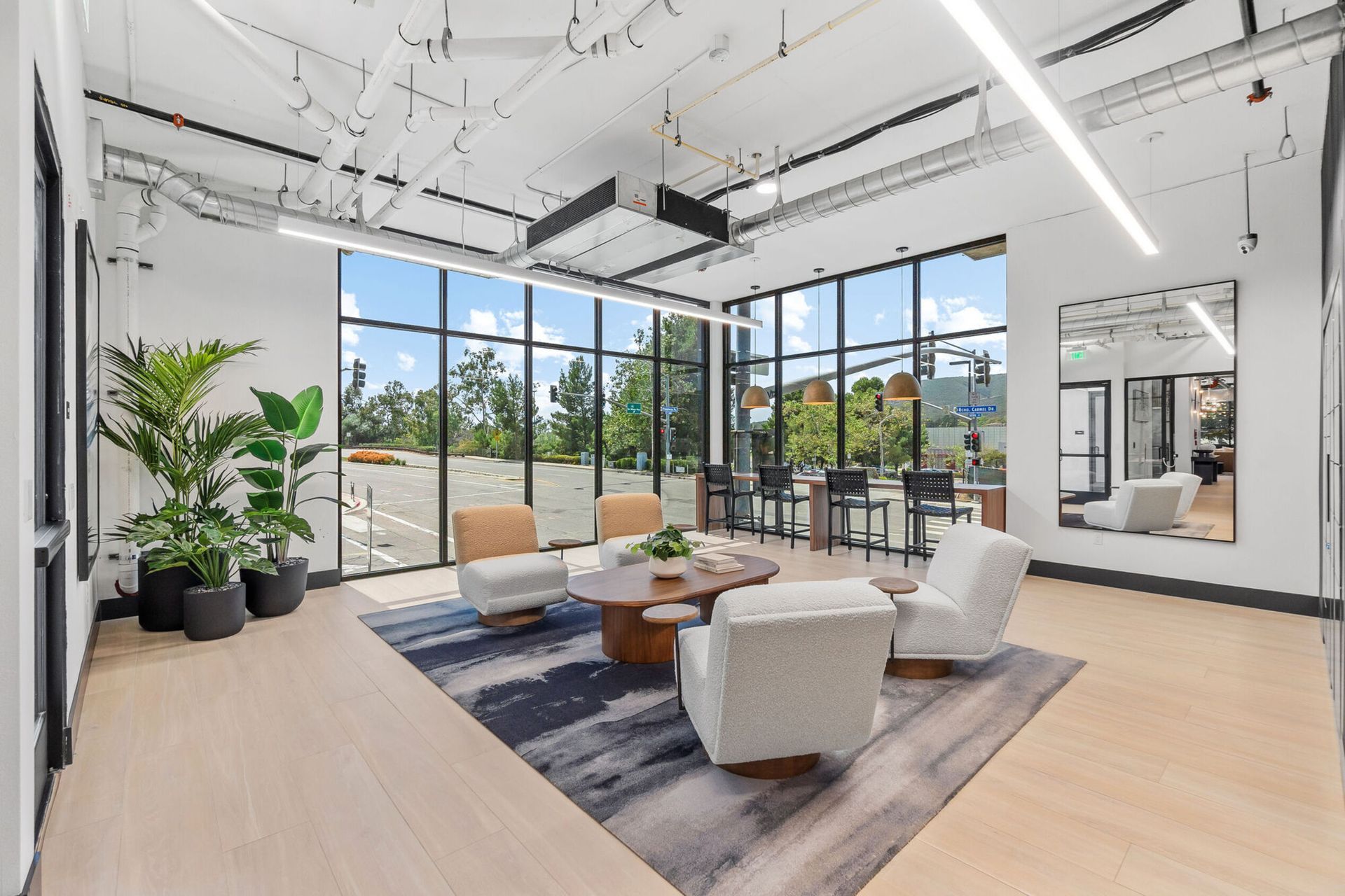 Bright office lounge with large windows, modern furniture, and potted plants.