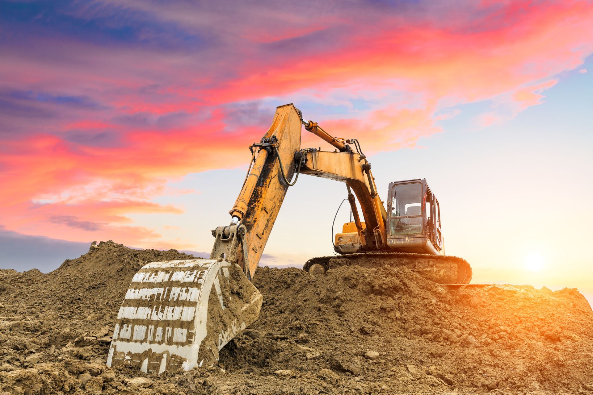 Construction site with orange cones, black cables in trench, and heavy machinery.