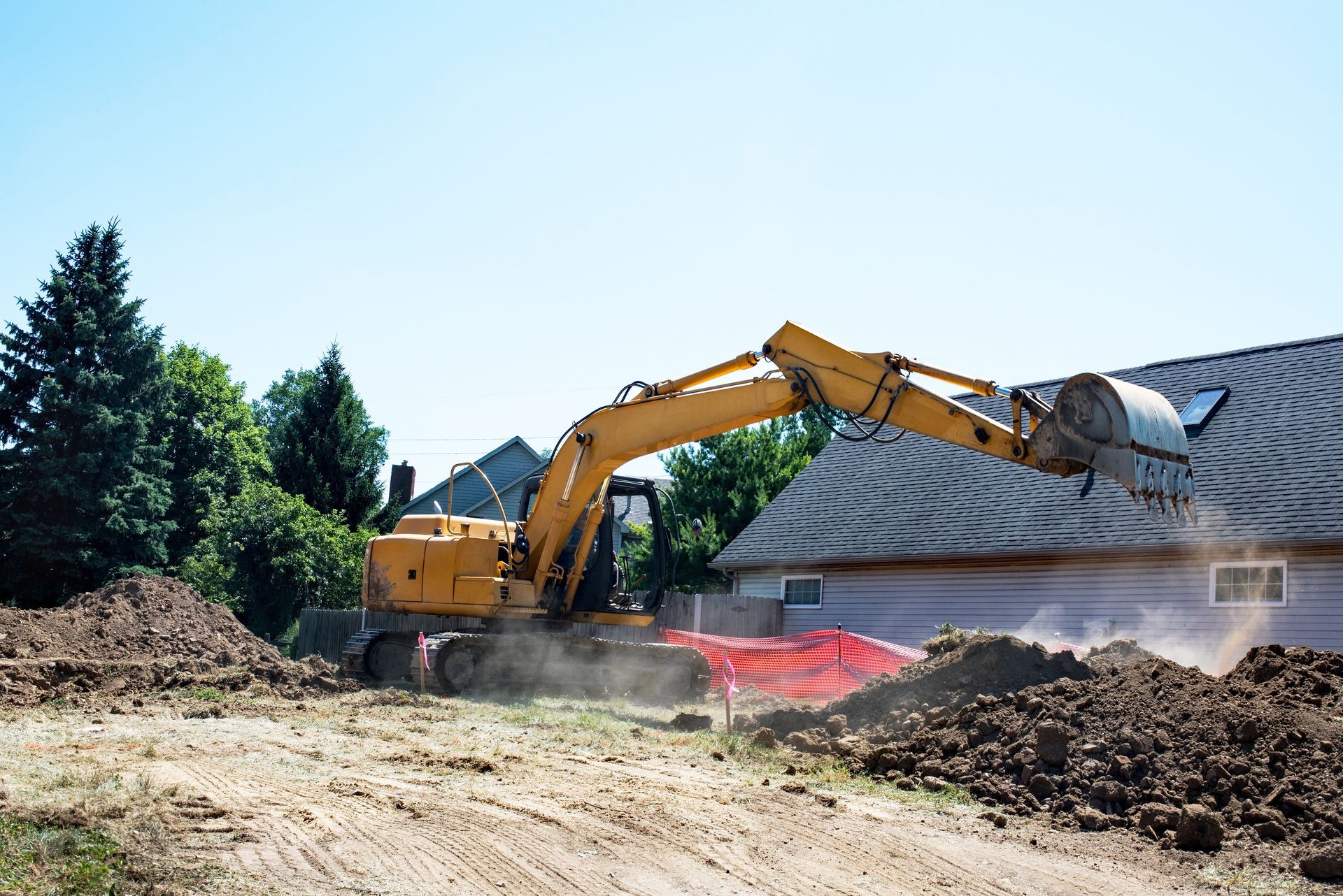 Yellow excavator digging trench for pipe in backyard.