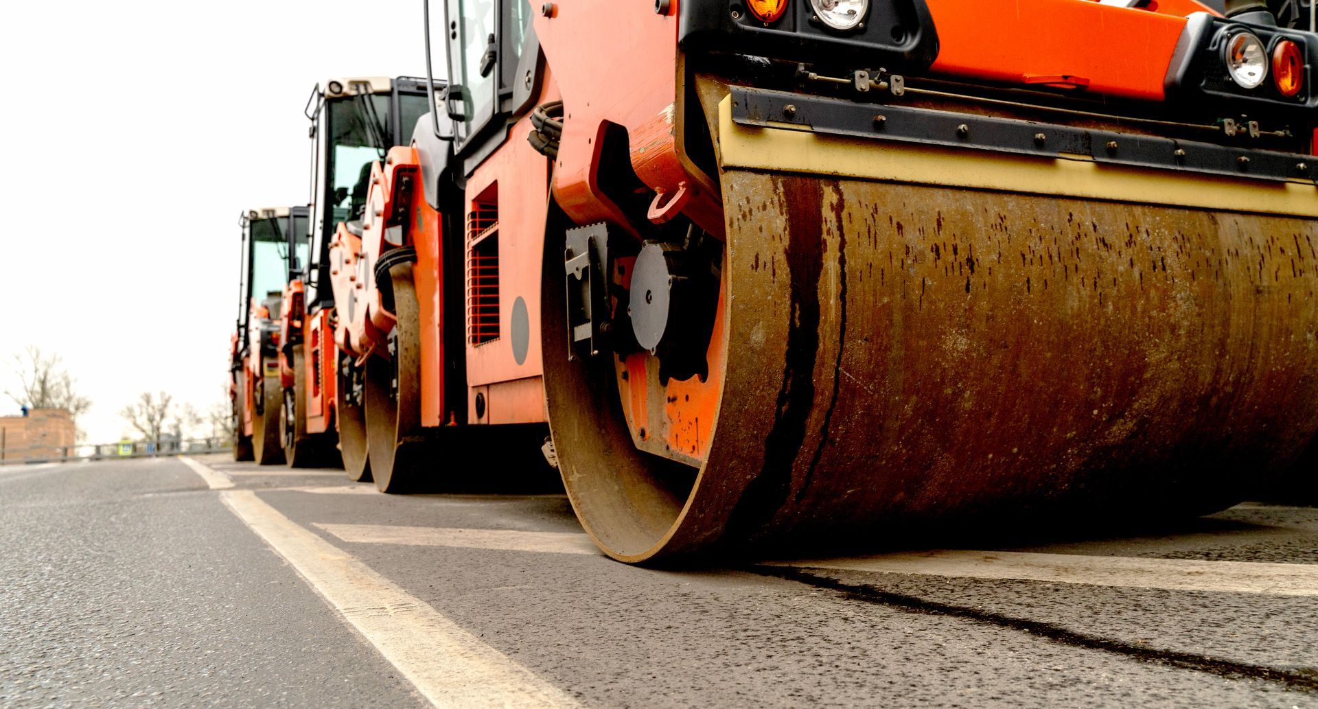Orange road roller compacting asphalt on a road with other machinery in the background. Orange road roller compacting asphalt on a road with other machinery in the background.