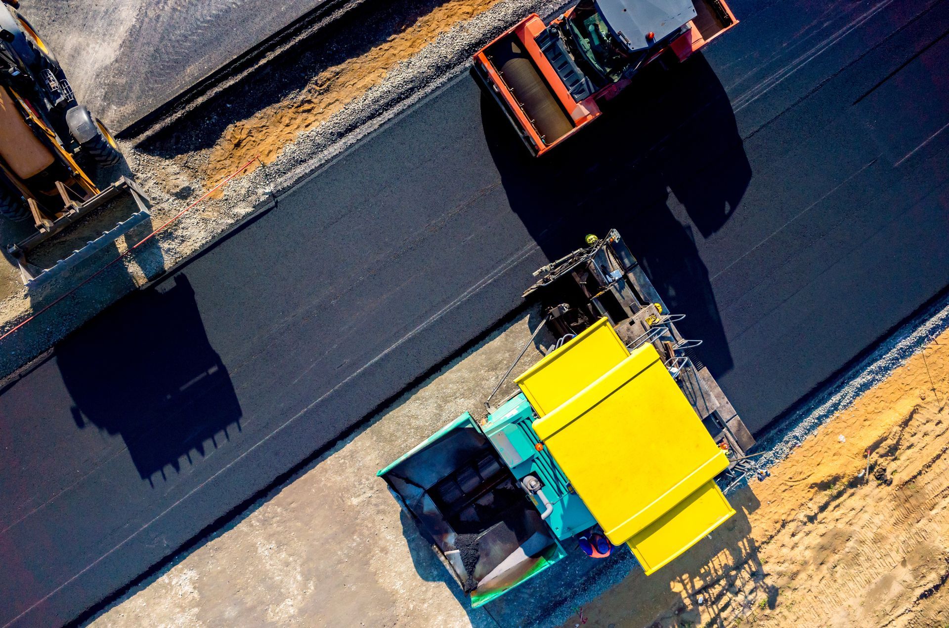Overhead view of road construction; paving machine and roller compacting asphalt.