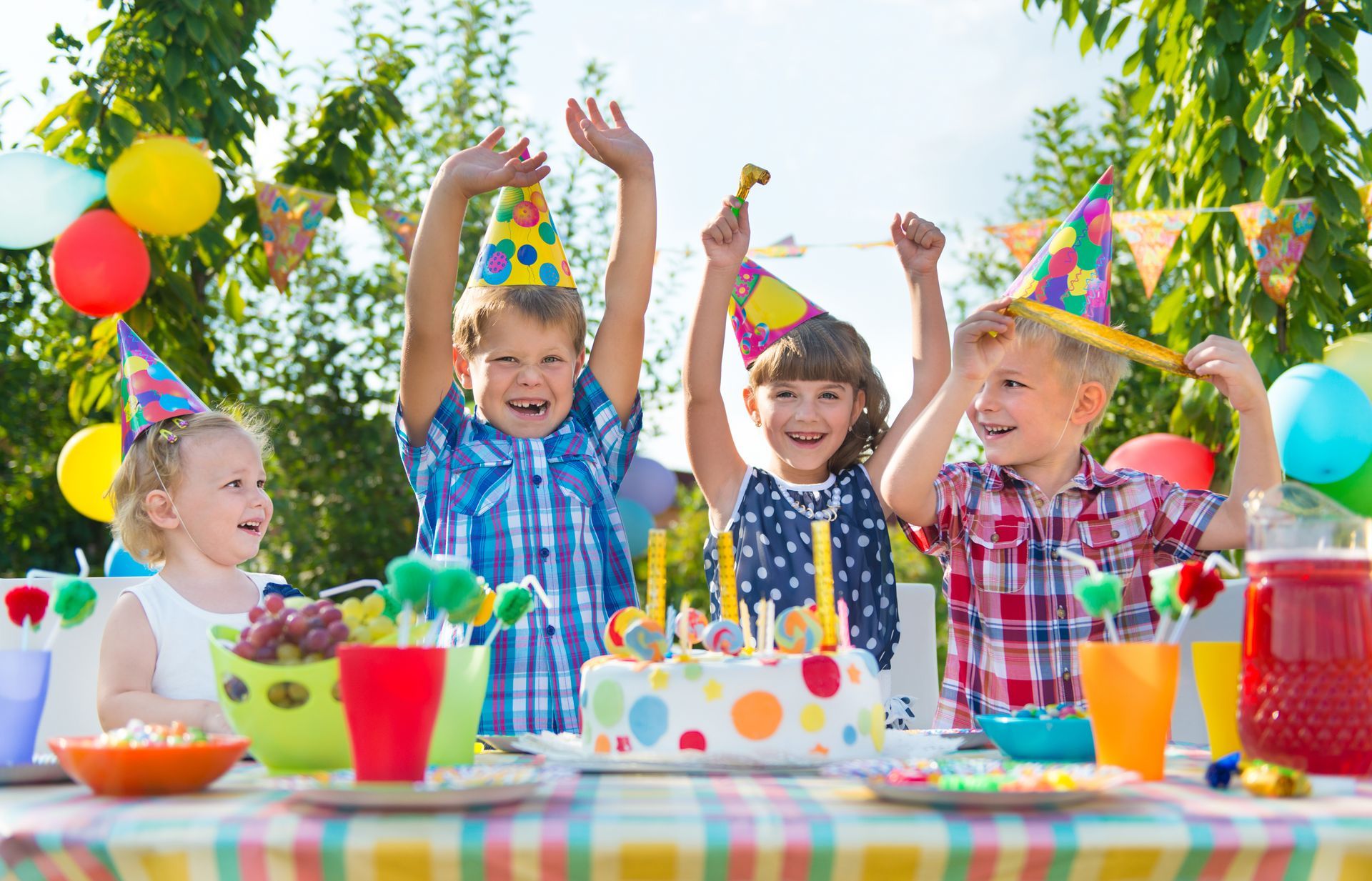 A group of children are sitting at a table with a birthday cake and balloons.