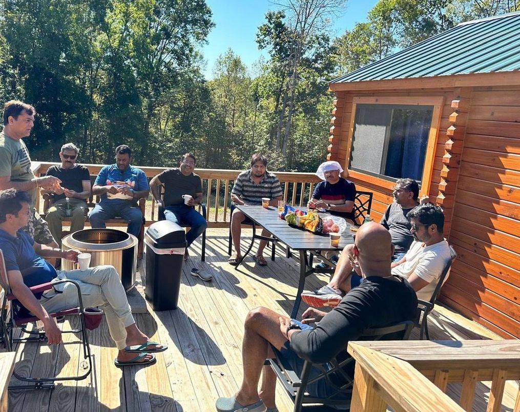 A group of men are sitting around a table on a deck.
