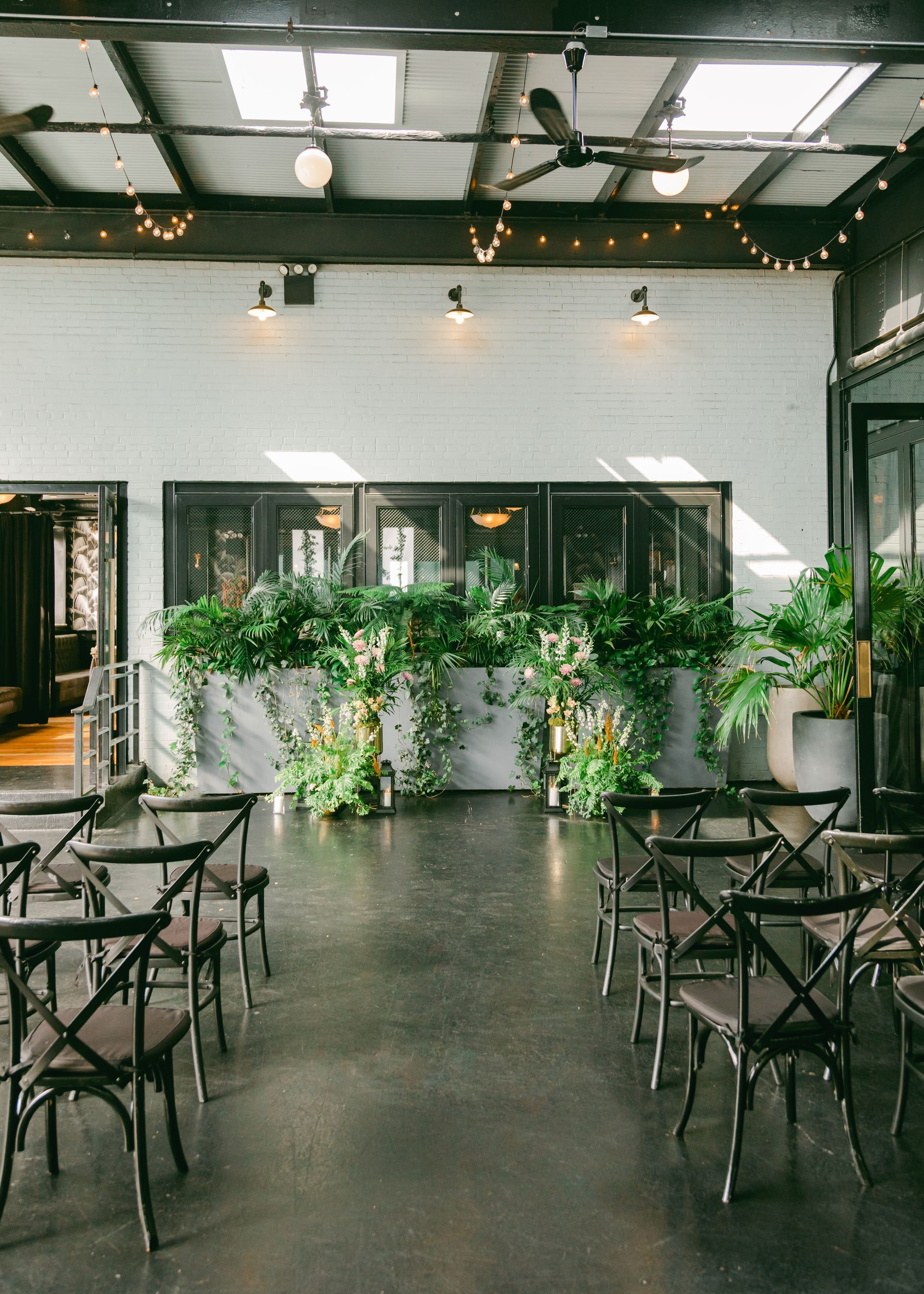 Empty indoor event hall with chairs, plants, and string lights under a high ceiling Empty indoor event hall with chairs, plants, and string lights under a high ceiling