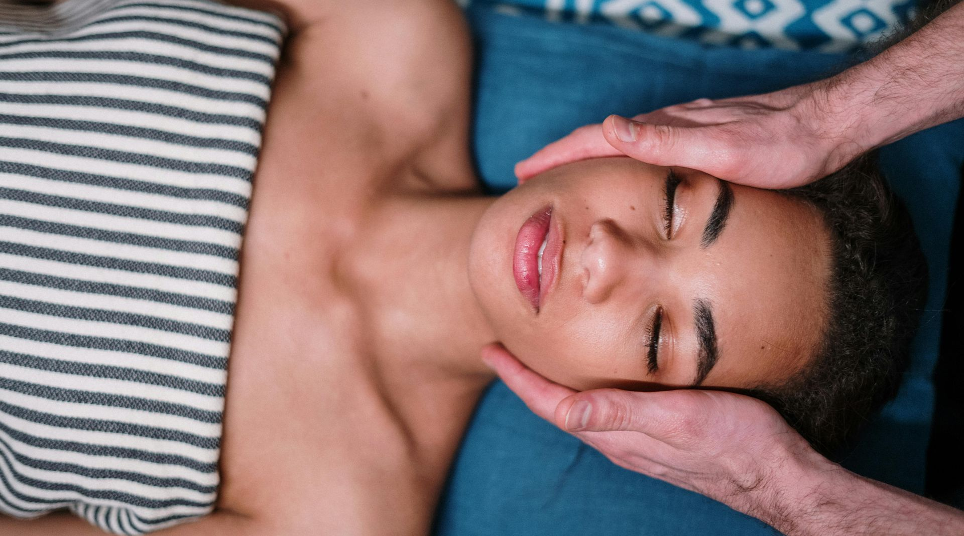 Person receiving facial massage; hands on face, eyes closed.