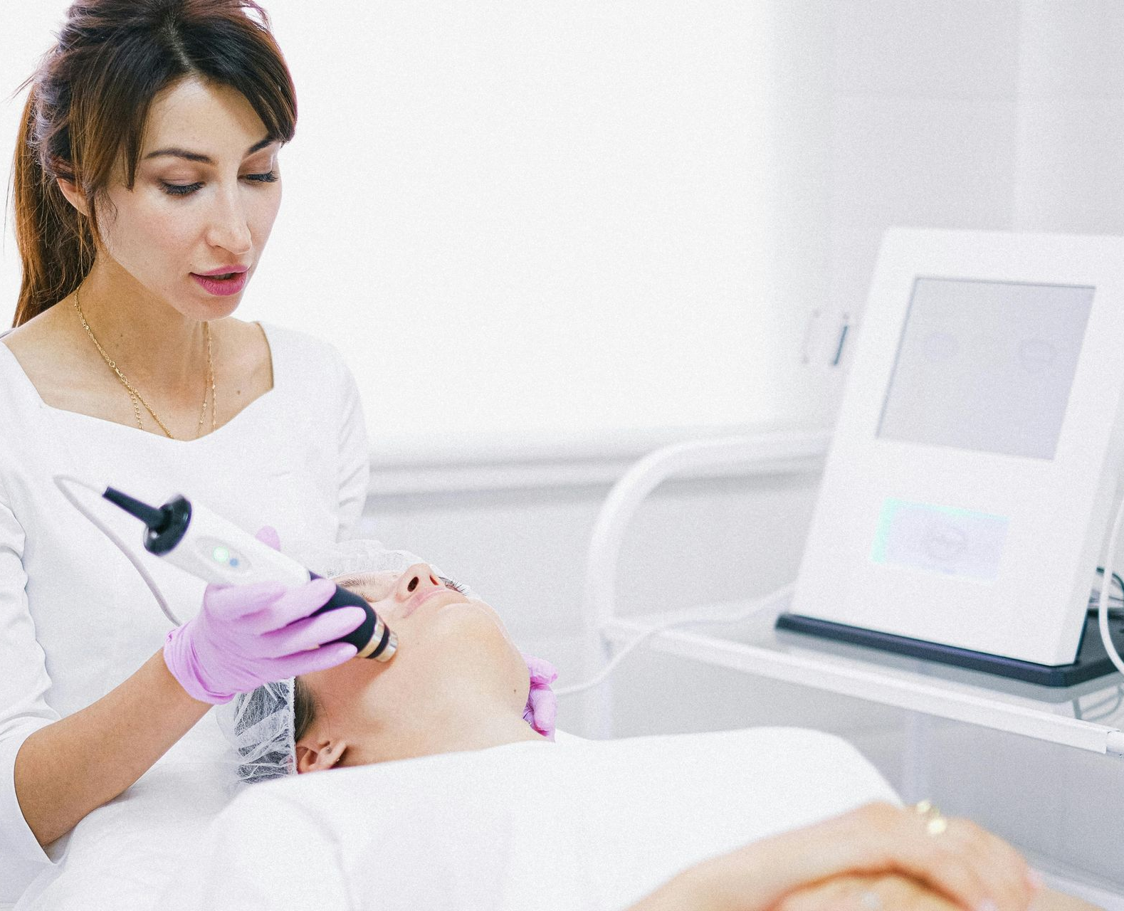 Beautician performing facial treatment with a handheld device on a client in a clinic.