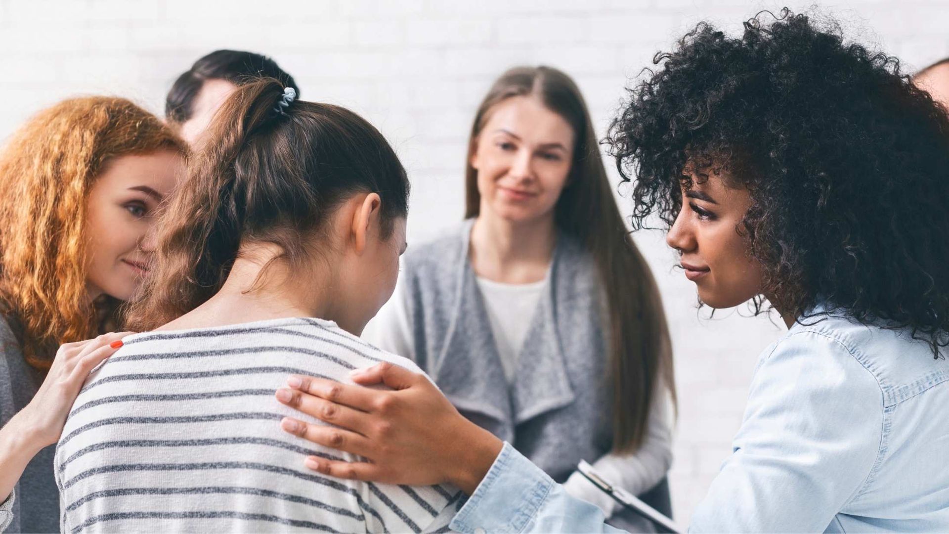 Group members offer supportive comfort to a person sitting with their head bowed in a circle meeting.