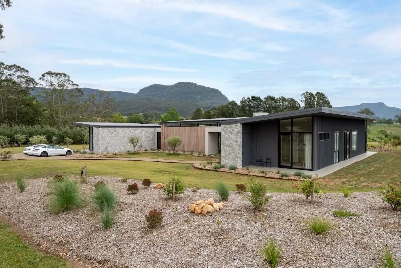 A Modern House Is Sitting In The Middle Of A Grassy Field With Mountains In The Background — That Painter Guy In South Nowra, NSW
