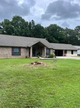 Single-story brick house with a wavy roof, green lawn, and cloudy sky; front porch visible