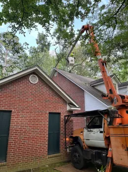 Orange crane lifting a white truck beside a brick house under trees