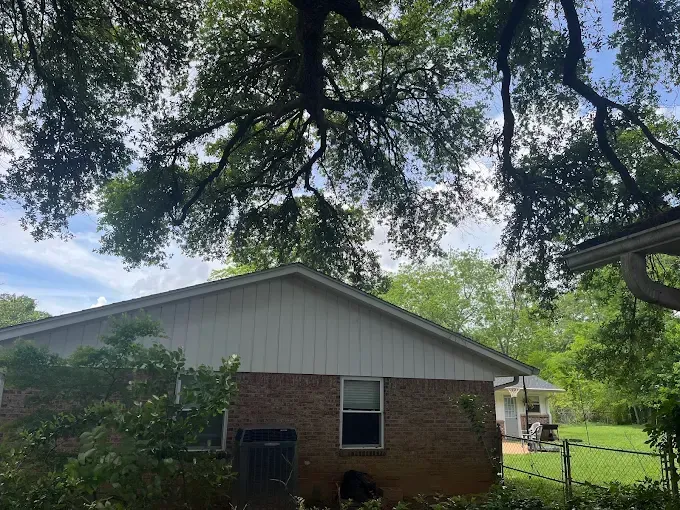 Brick house with white gable siding, framed by large tree branches and a green backyard.