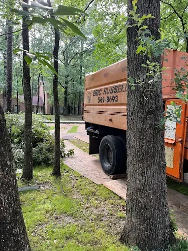 Orange utility truck on a forest path beside trees and wet grass