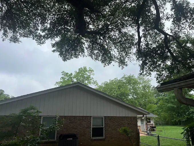 Brick house under large tree branches on a cloudy day