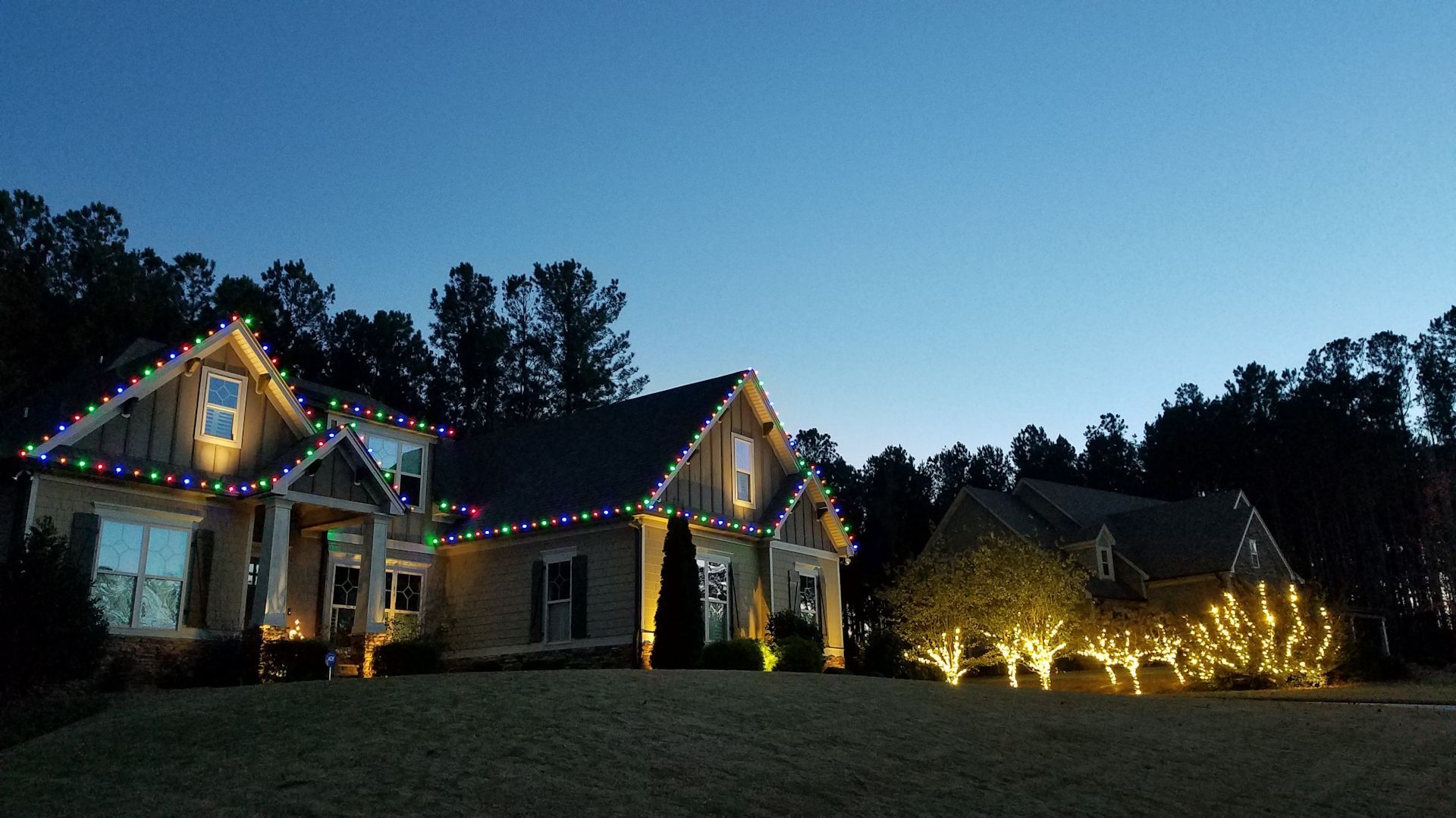 Suburban houses decorated with colorful holiday lights at dusk under a dark blue sky