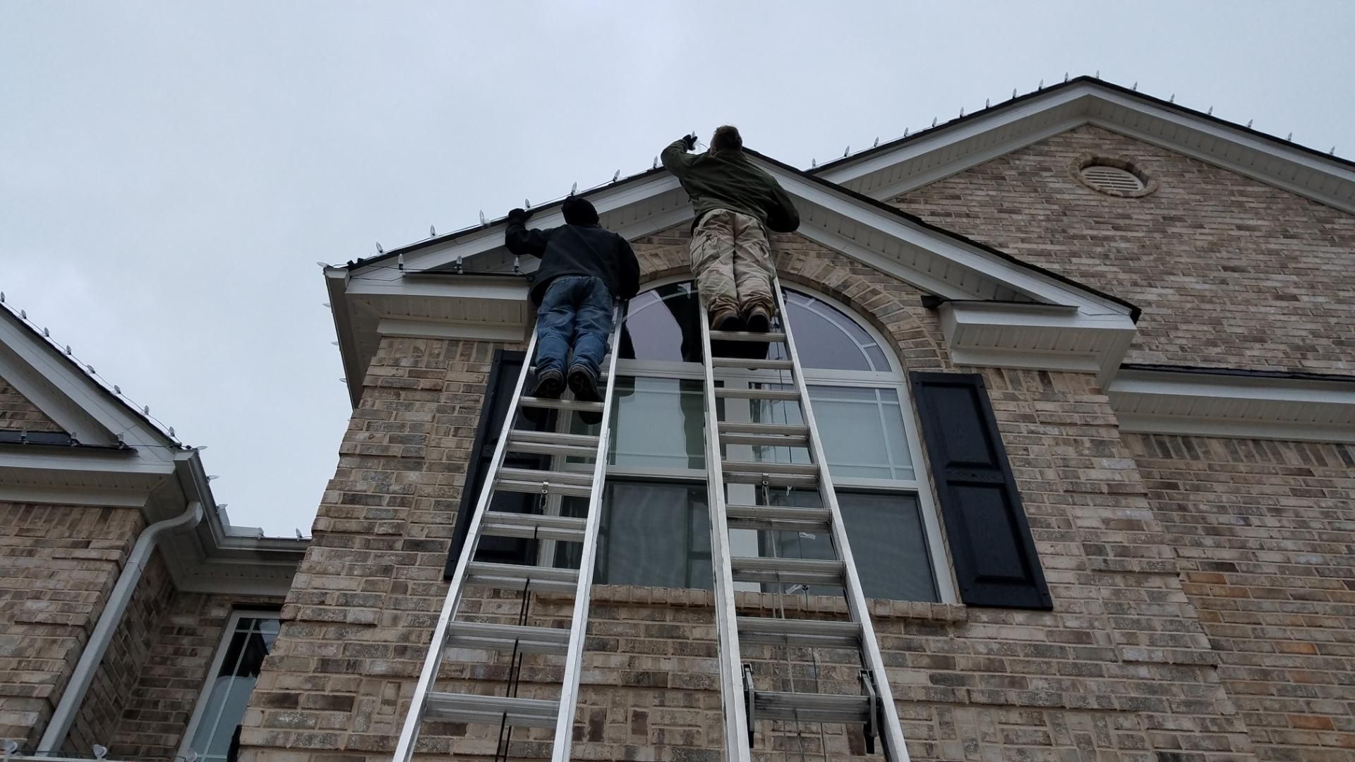 Two workers on ladders fixing the roof of a brick house