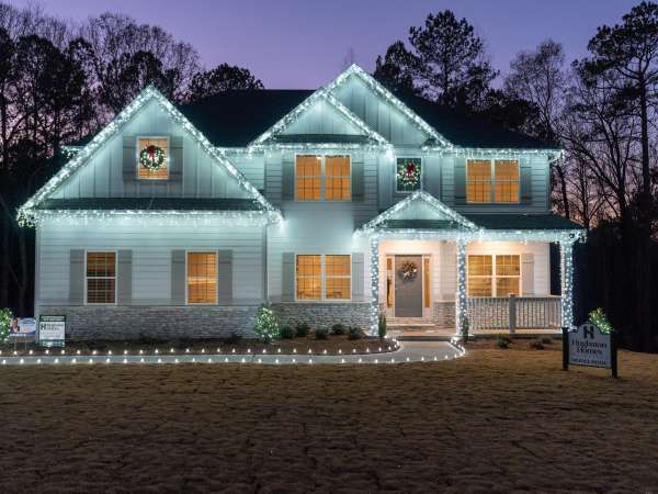 White house outlined in holiday lights at dusk, with lit windows and a sign in the front yard.