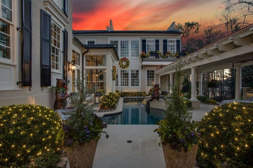 Courtyard pool at sunset between white stucco buildings, with lit shrubs and a pergola walkway