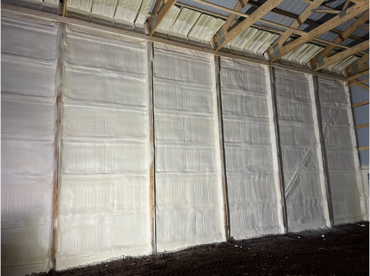 Interior of a building with white insulation covering the walls. Wooden beams are visible at the top.