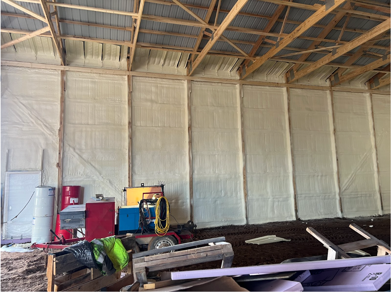Interior view of a barn with light-colored spray foam insulation on the walls. 
