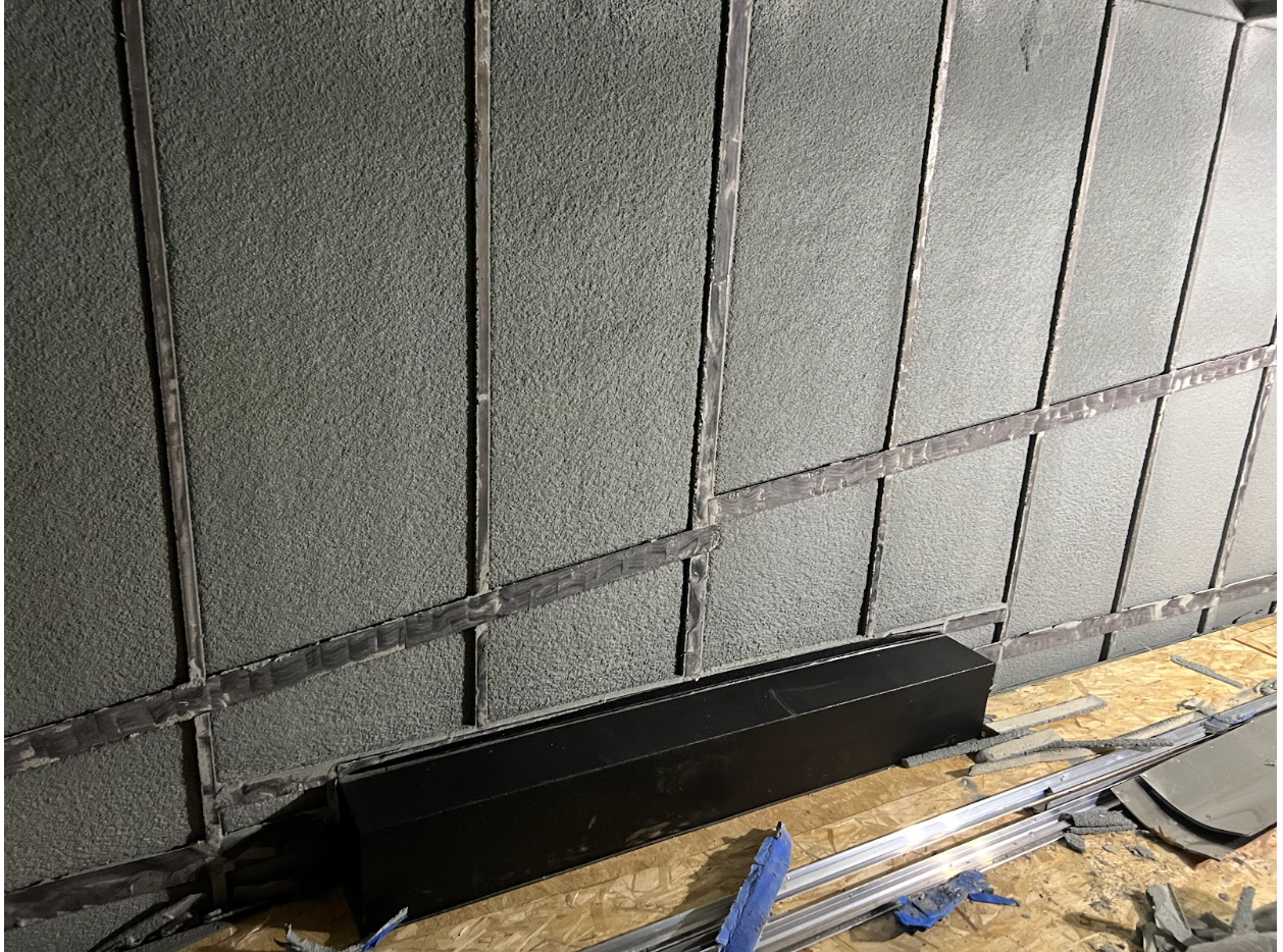 Gray soundproofing panels with black trim installed on a wall, with a black rectangular object below.