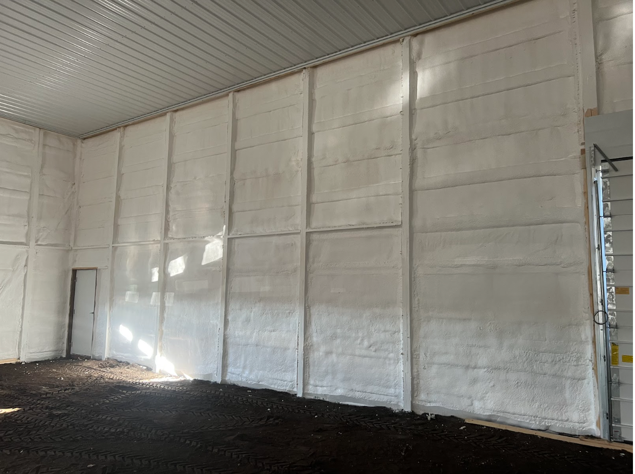 Interior of a building with white foam insulation on the walls. The floor is covered in dark soil.