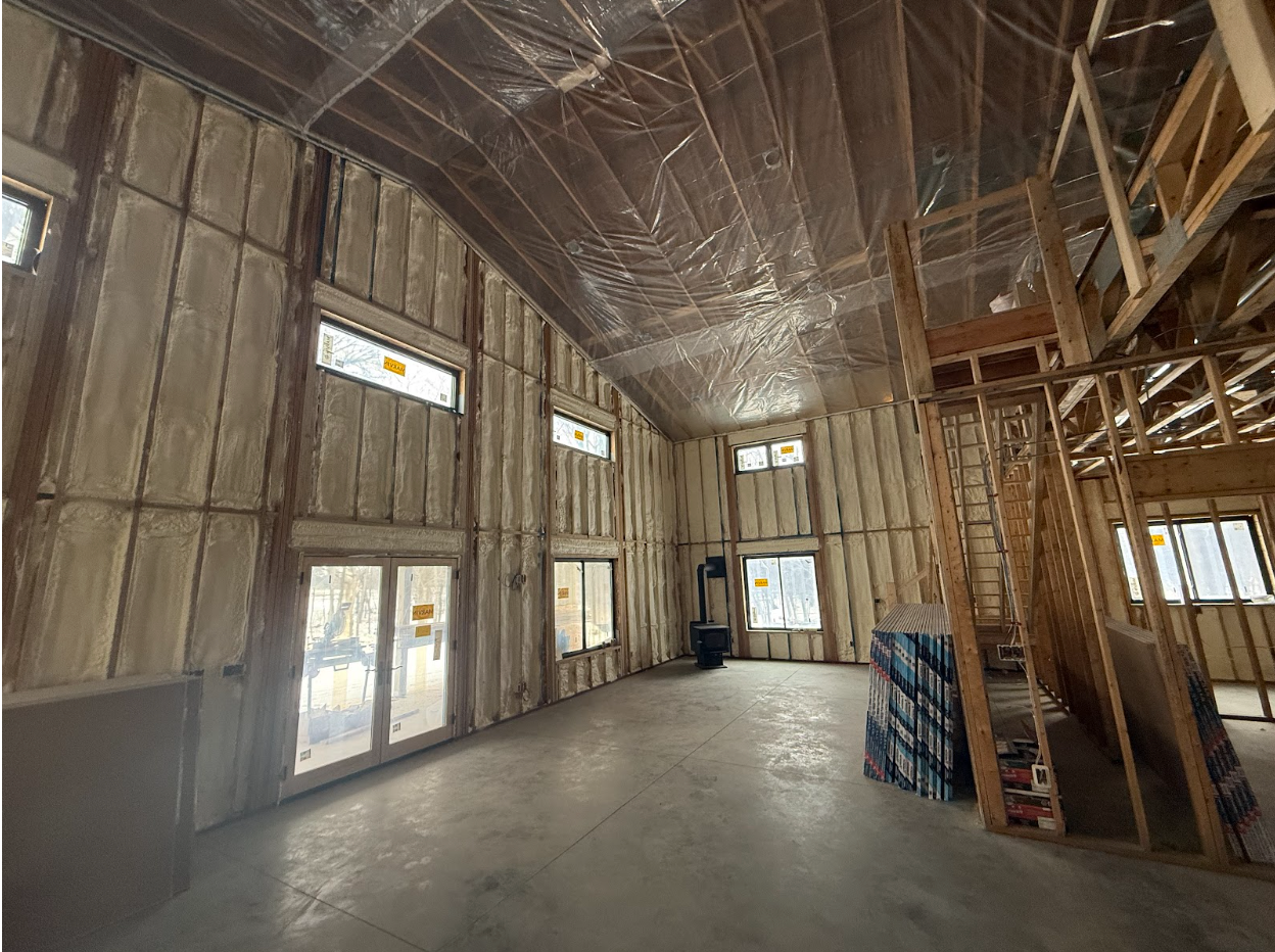 Interior of a new building under construction, spray foam insulation on walls, clear plastic covering ceiling.