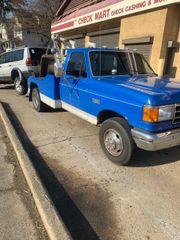 Blue pickup truck parked on a sidewalk outside a repair shop, with a white SUV behind it.