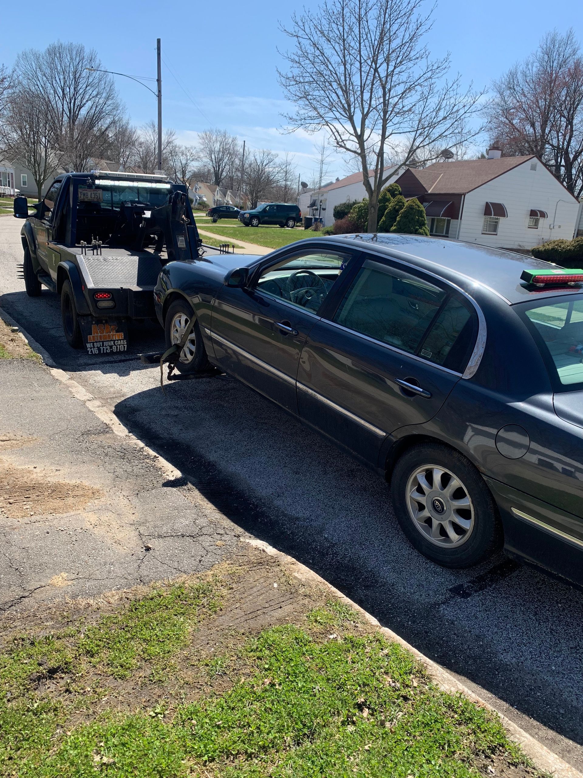 Tow truck loading a dark sedan on a sunny residential street