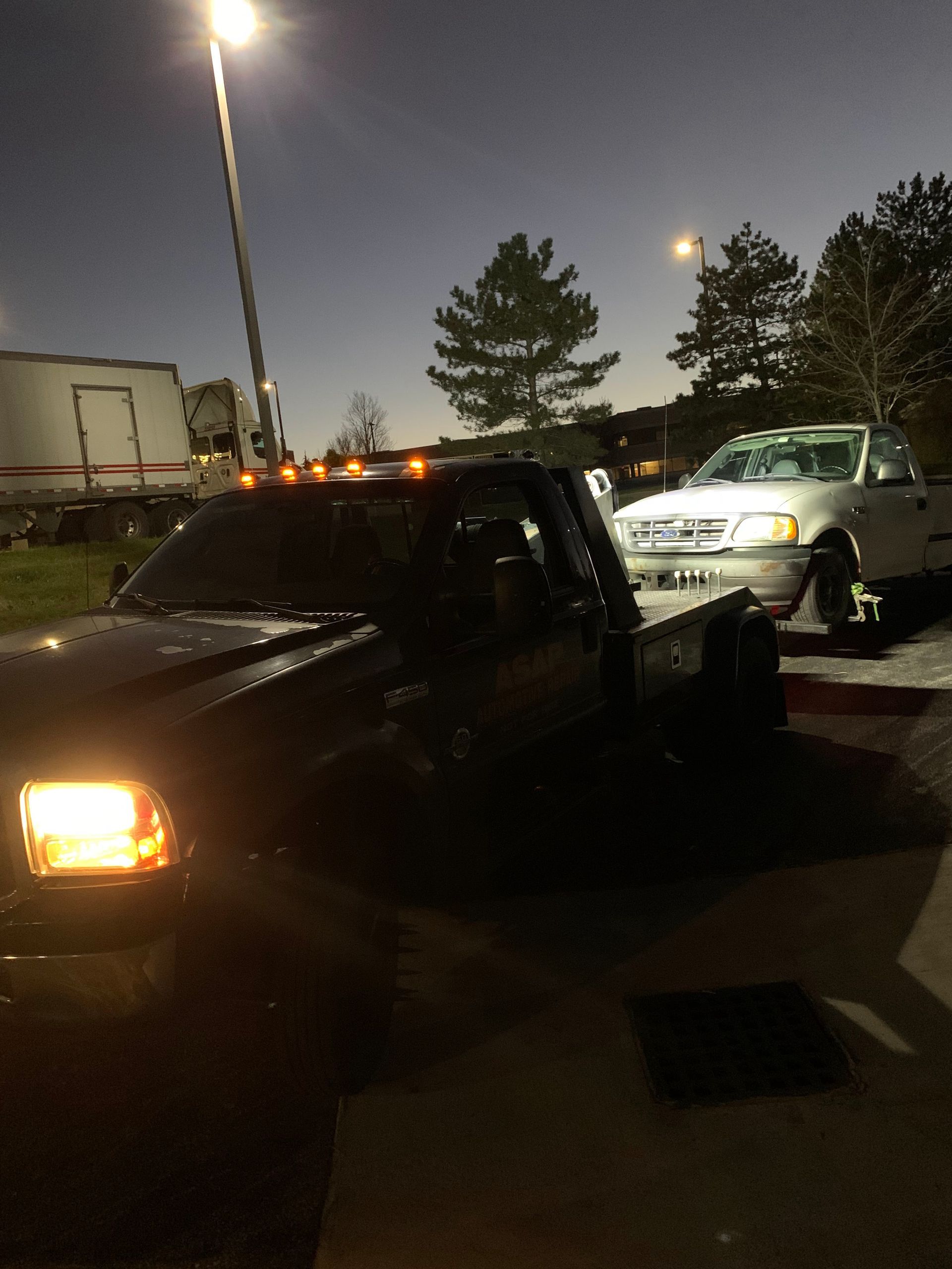 Tow trucks at night beside a white car in a parking lot