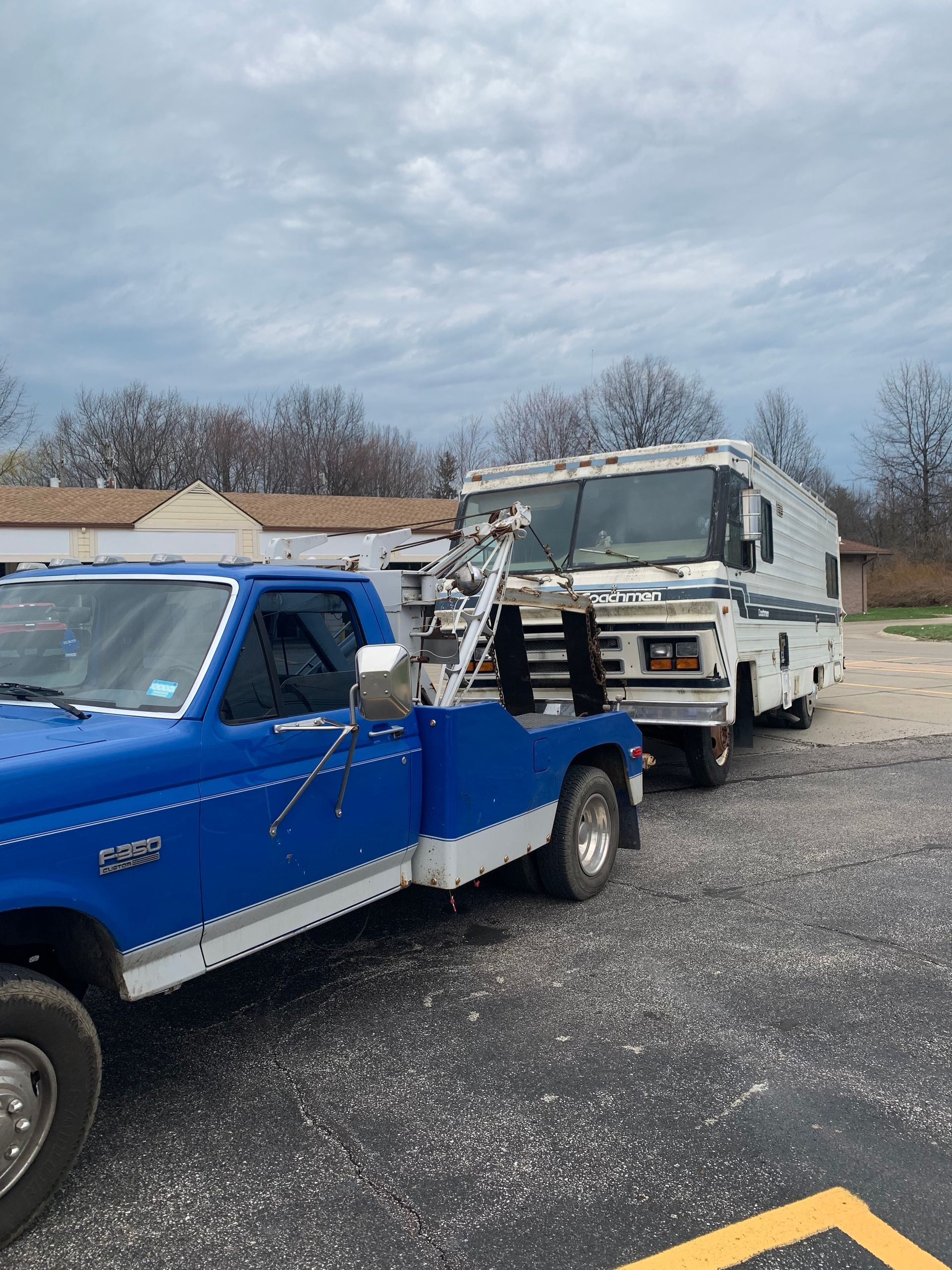 Blue pickup truck towing a white tow truck in a gravel lot under cloudy skies