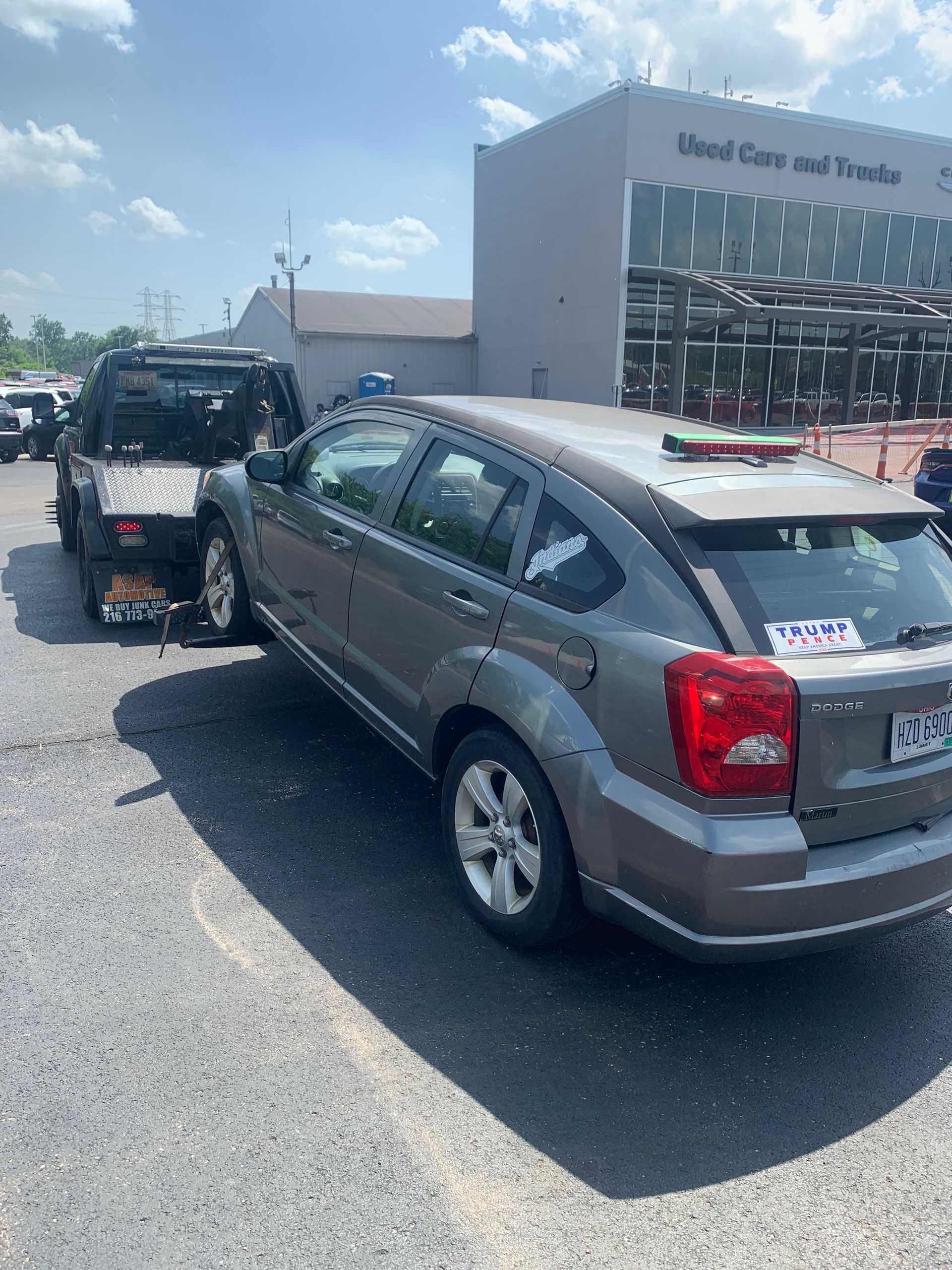 Gray SUV towing a black off-road vehicle in a used car lot under bright sun
