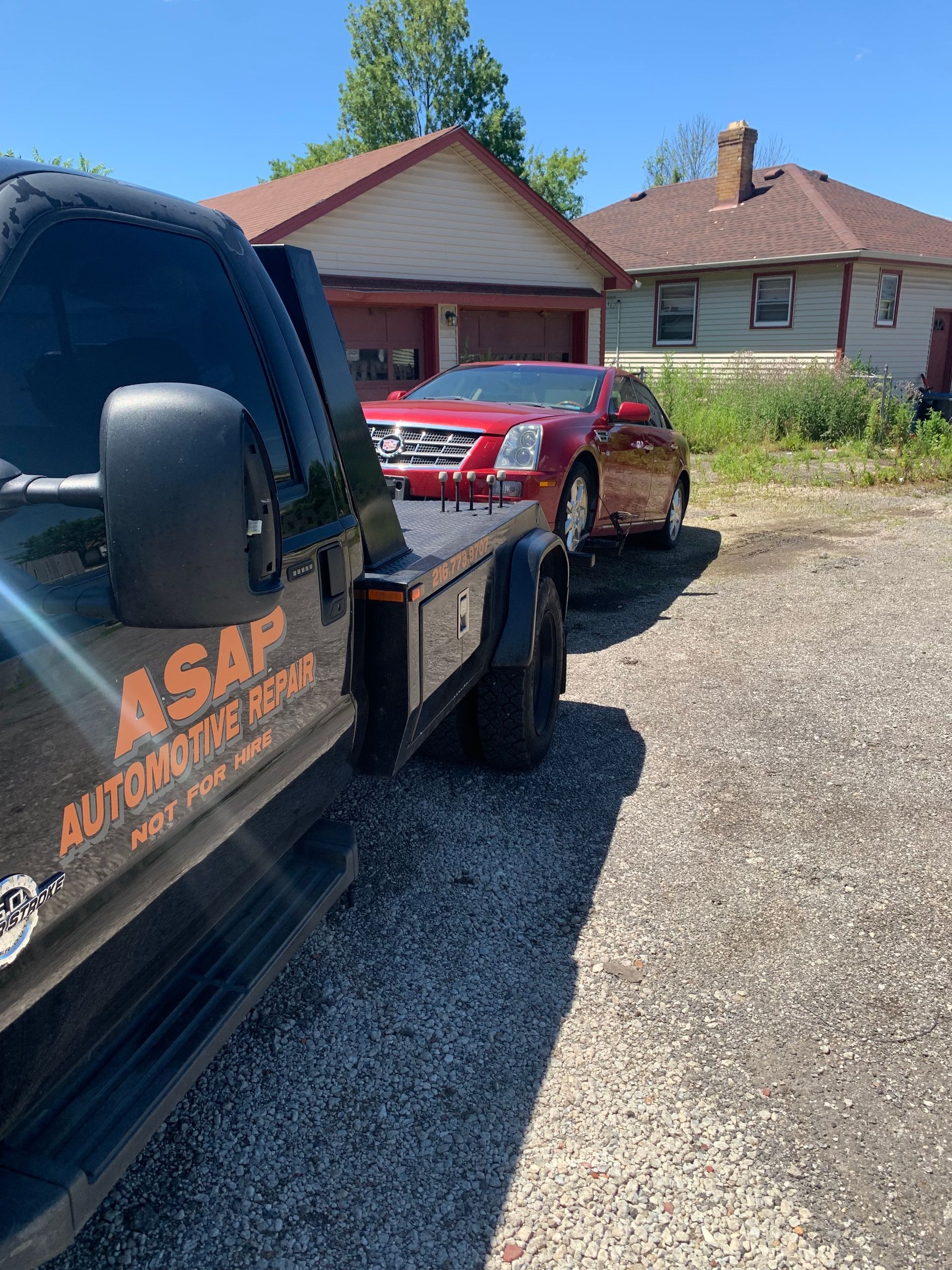 Tow truck hauling a red car in front of suburban houses on a gravel driveway