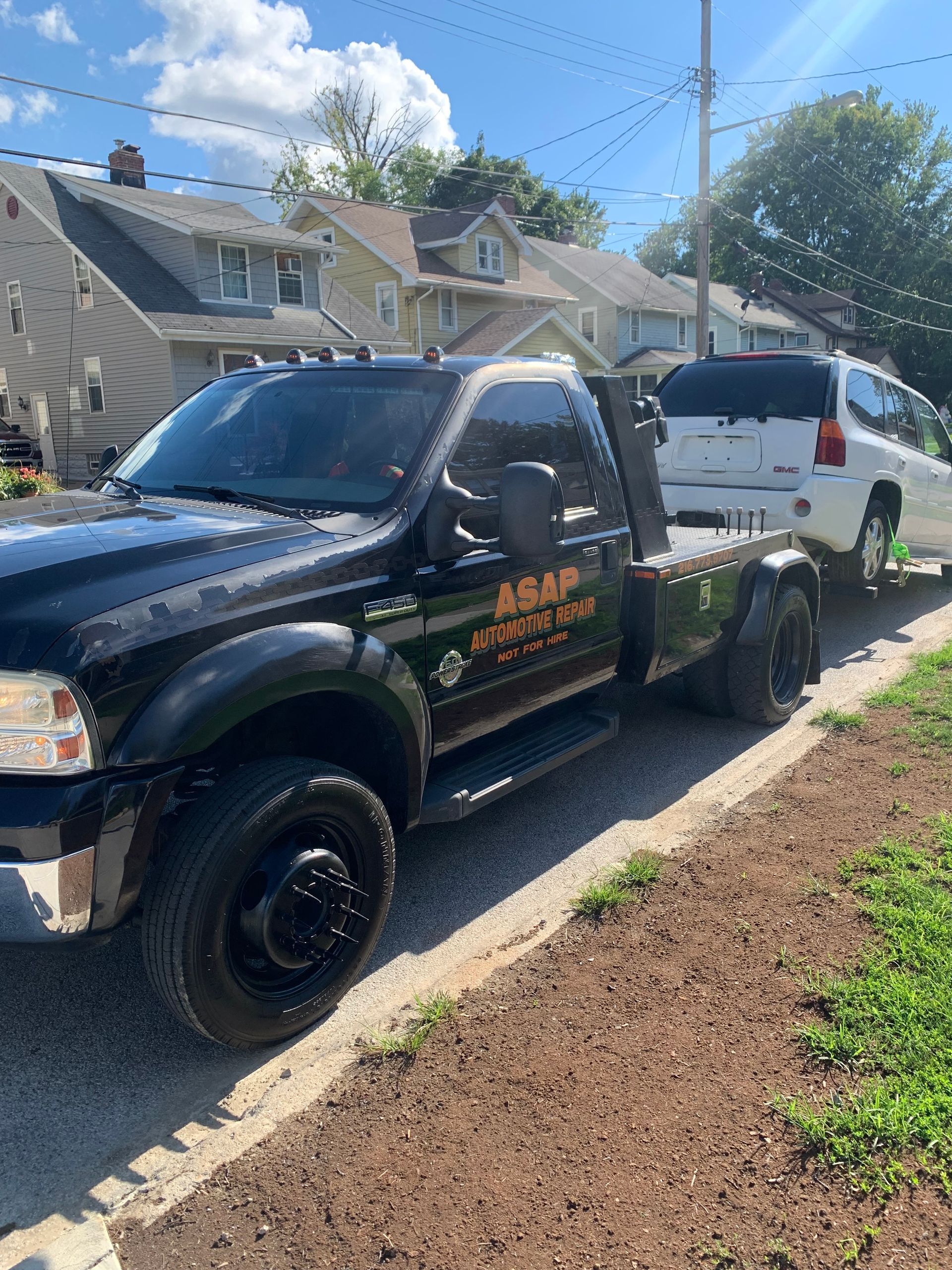Black pickup truck towing a white SUV on a residential street under a partly cloudy sky