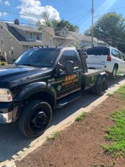 Black pickup truck towing a white SUV on a suburban street, with houses and blue sky in the background