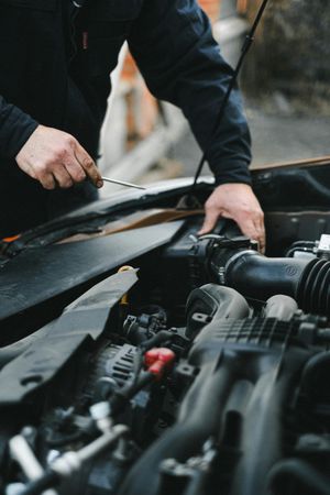 Mechanic working under an open car hood in a repair shop