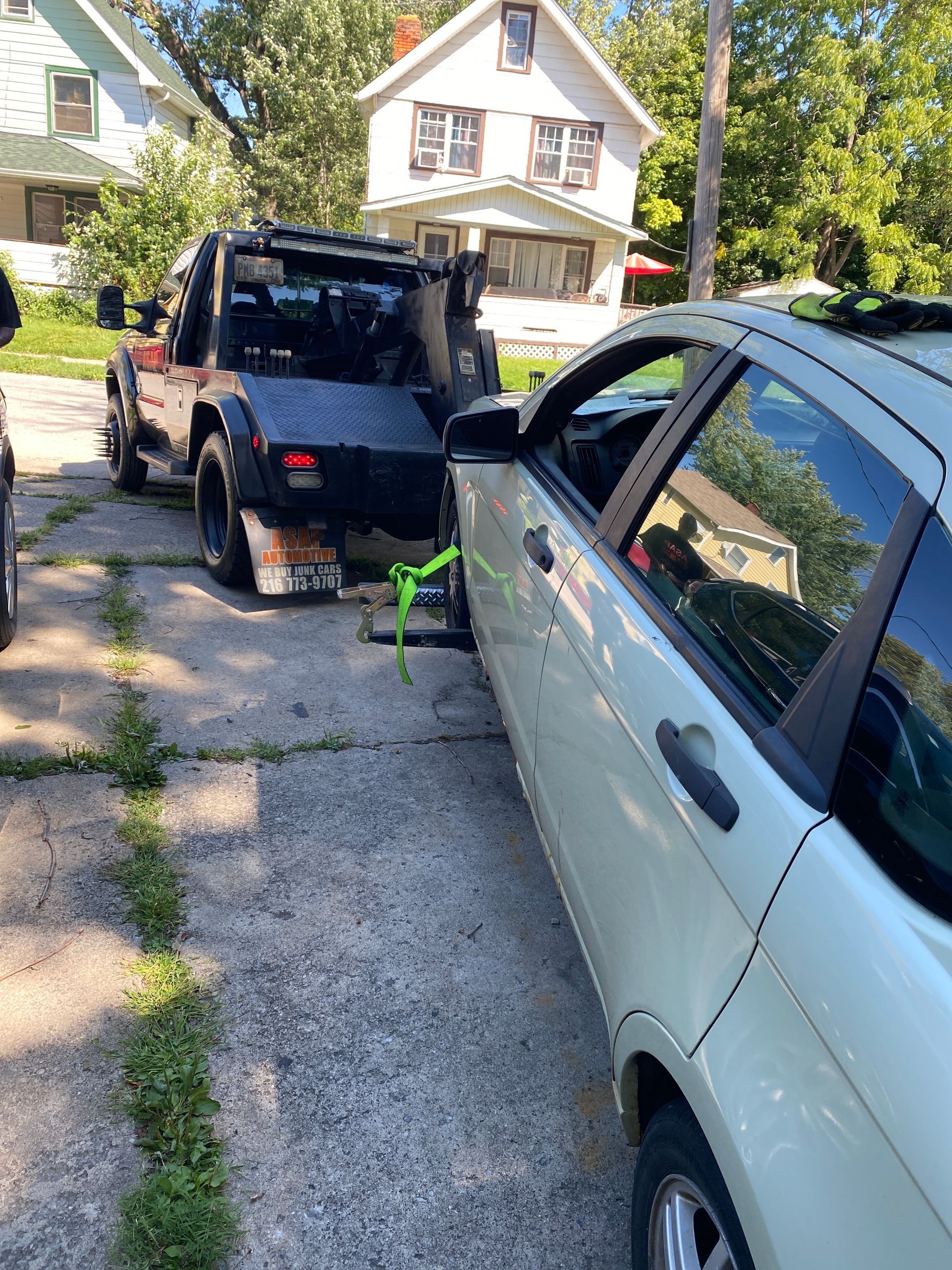 Car and black SUV parked in a driveway after a collision, with a green tow strap attached.