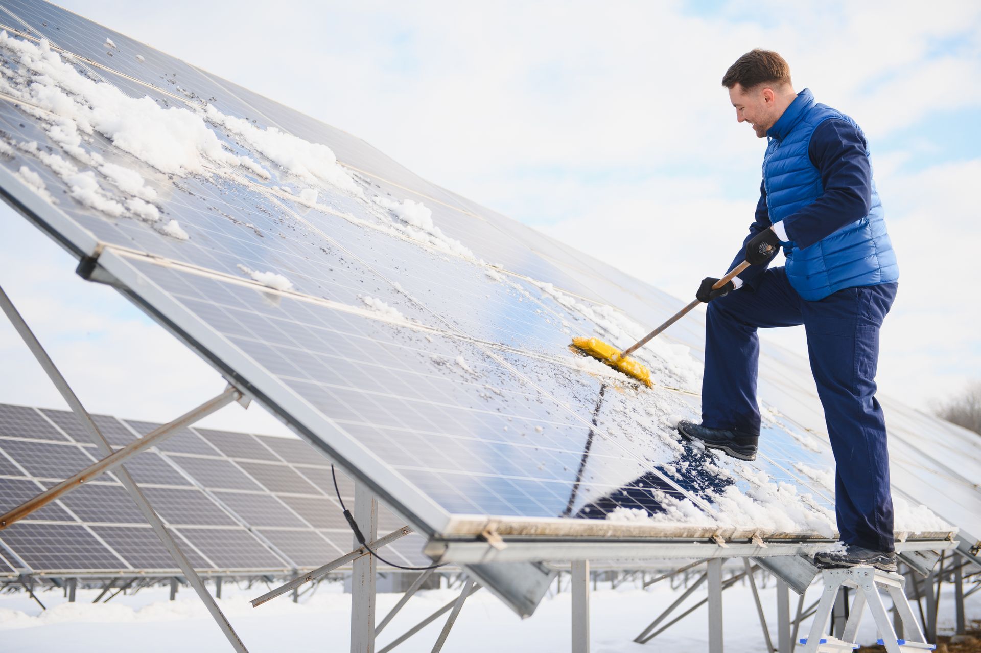 Arbeiter entfernt mit einem Besen Schnee von Solarpaneelen auf einem Dach.