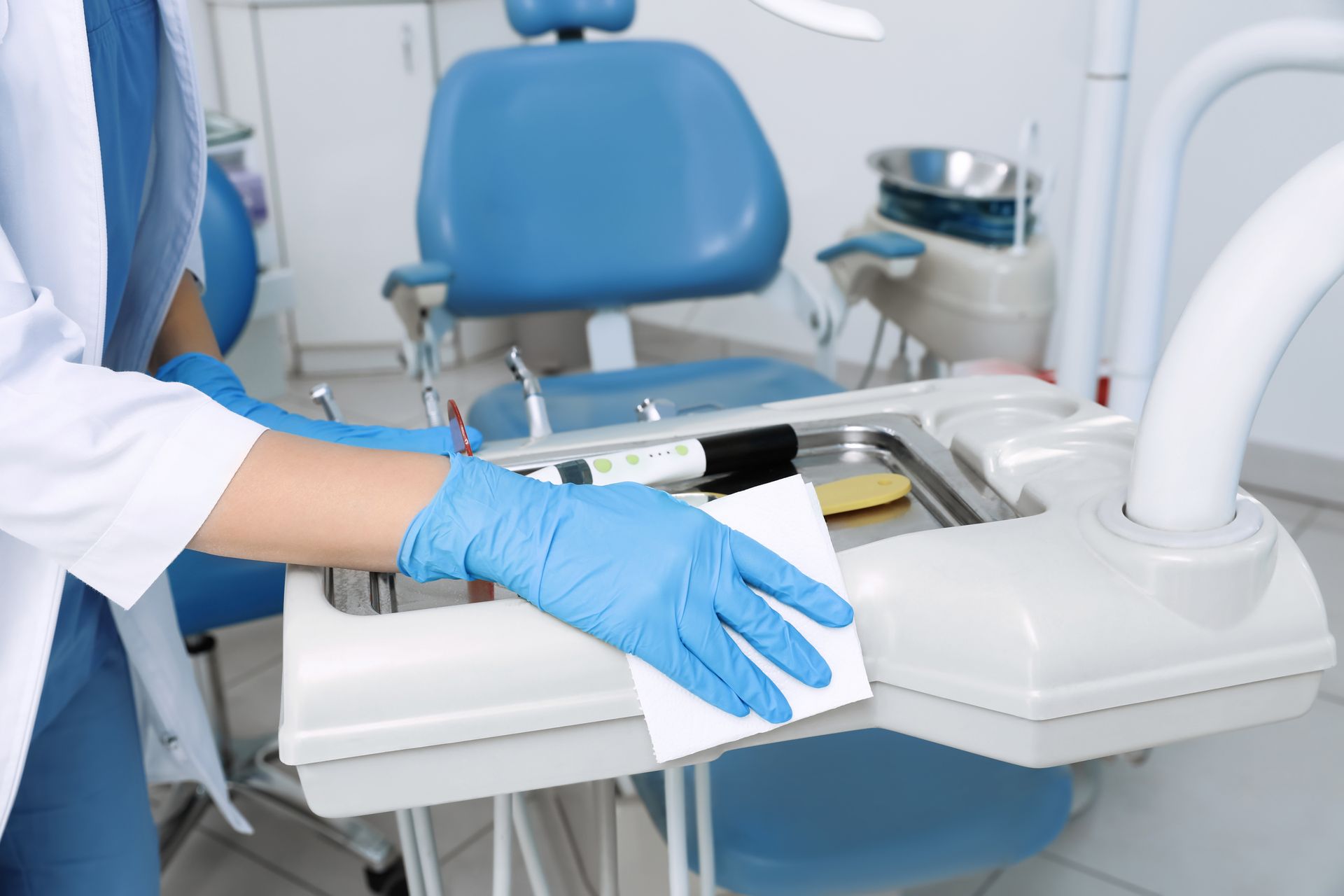 Ein Zahnarzt mit blauen Handschuhen justiert ein Zahntablett neben einem blauen Stuhl in einer Klinik.