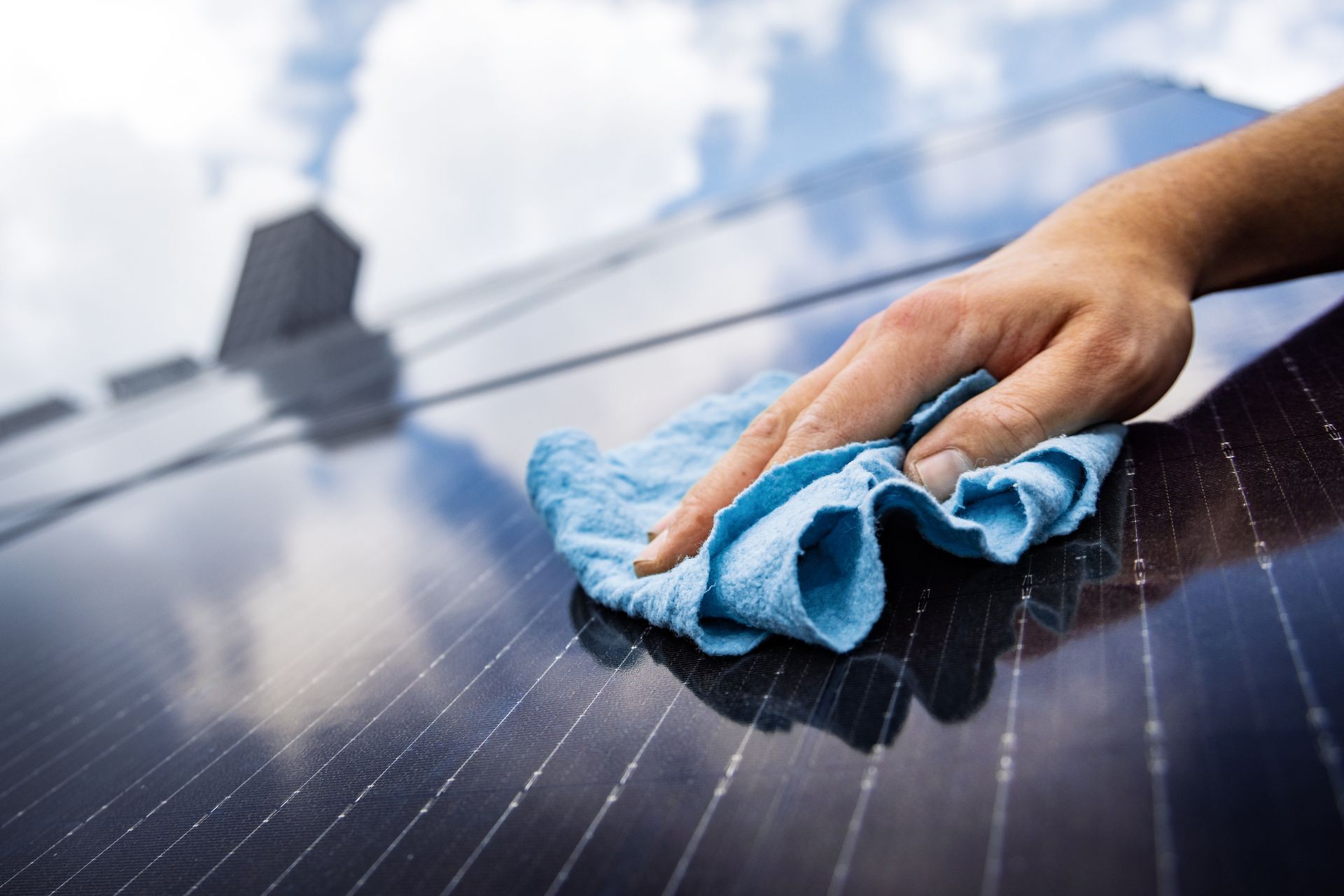 Unter strahlend blauem Himmel wischt man mit der Hand Staub von einem Solarpanel.
