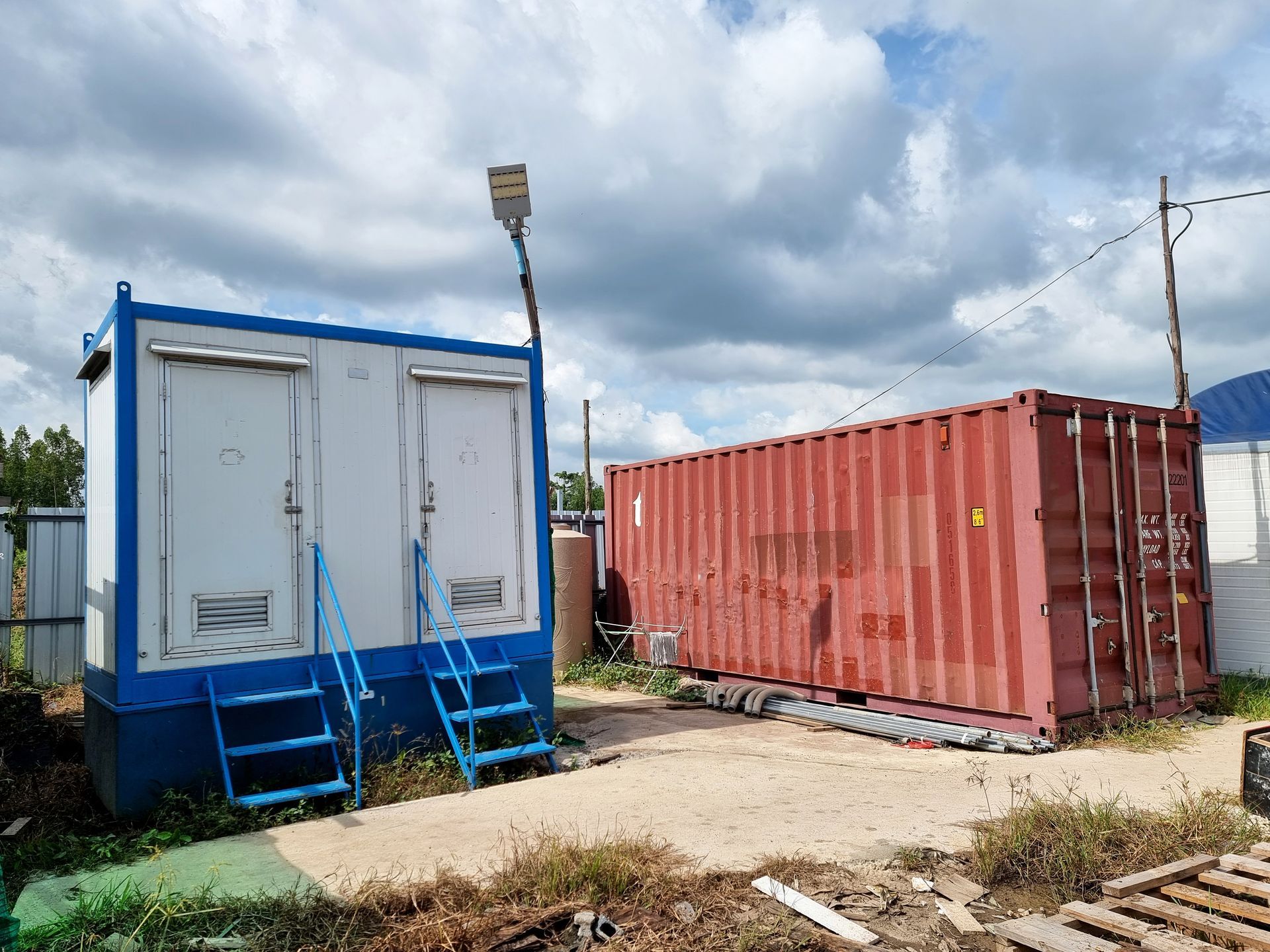 Blaues mobiles Büro mit Treppe neben einem roten Schiffscontainer unter einem bewölkten Himmel