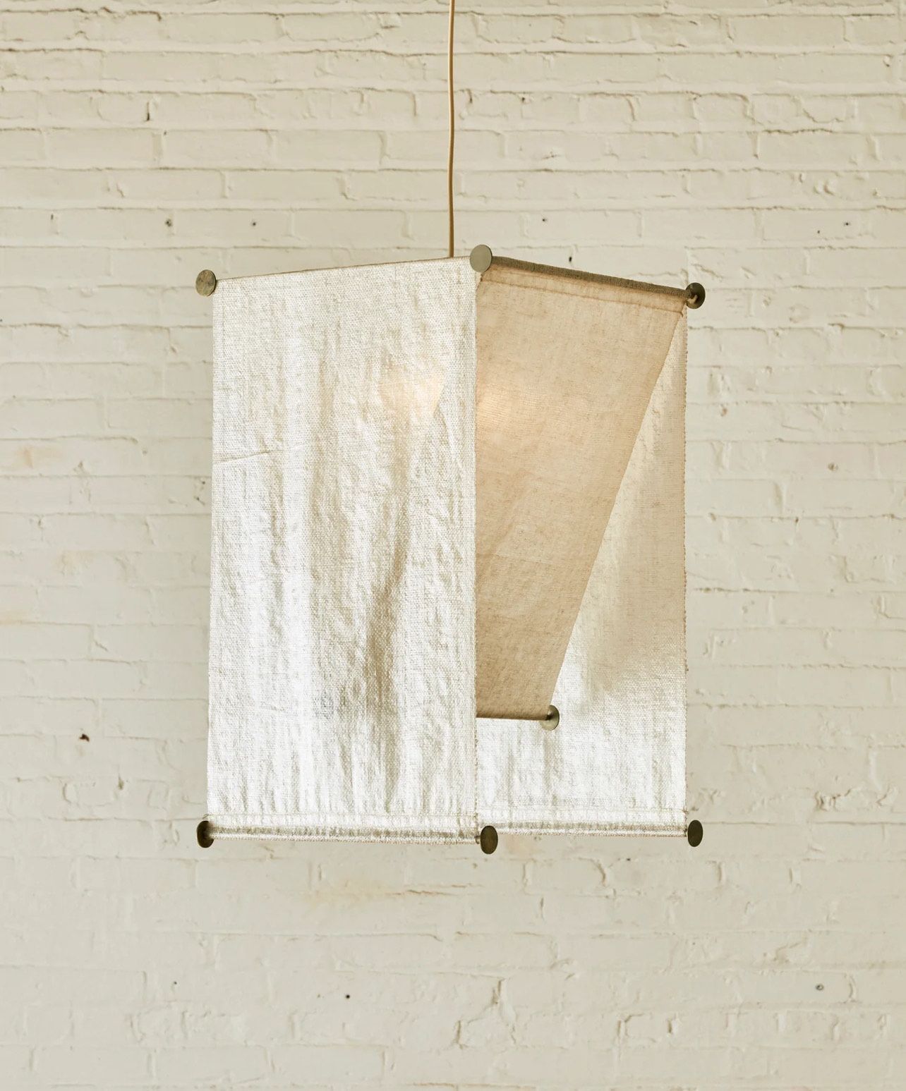 Square pendant lamp with textured white fabric sides, hanging against a white brick wall.