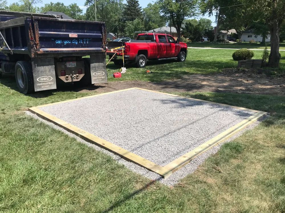 A dump truck is parked in the grass next to a concrete slab.