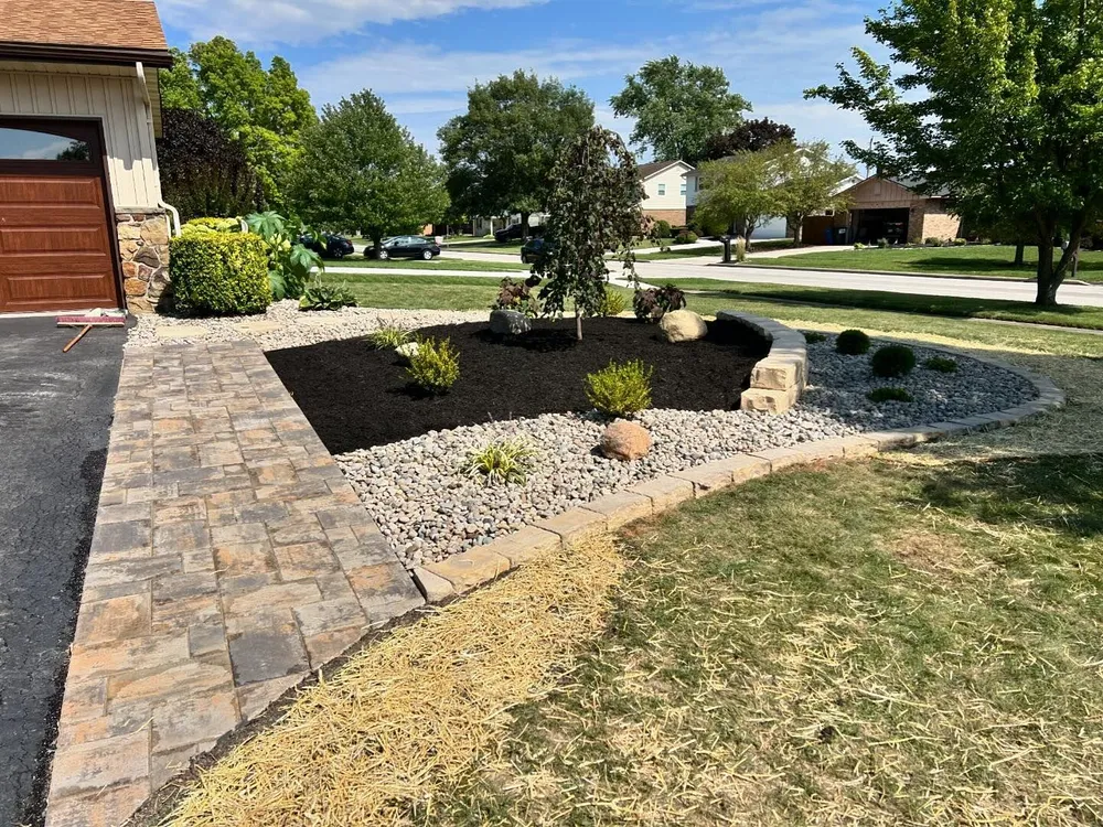 A driveway leading to a house with a garden in front of it.